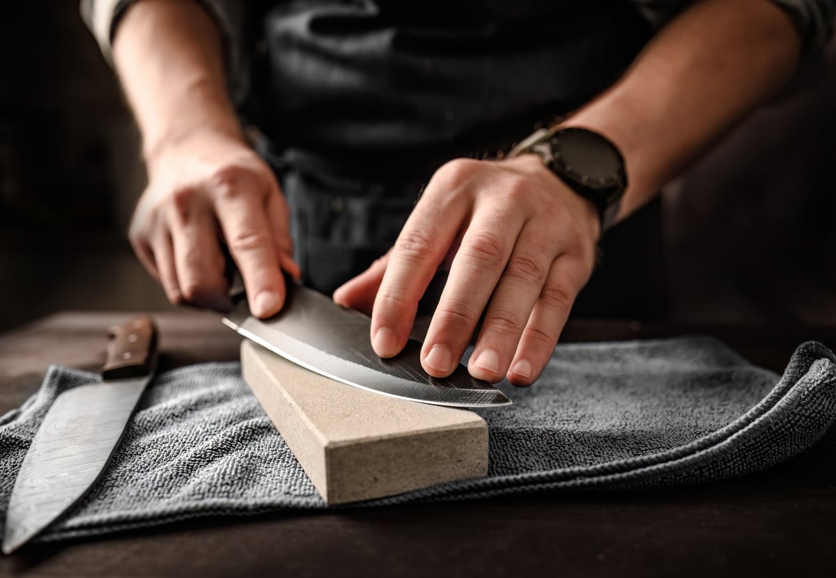 Master bladesmith hand sharpening a knife on a whetstone